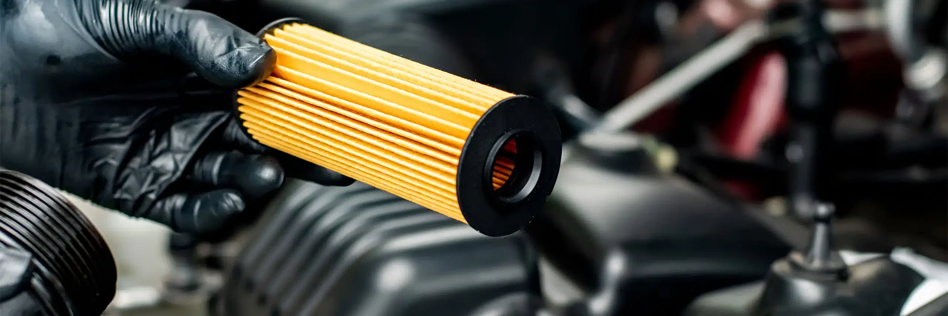 The worker is changing an oil filter.